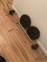 Full view of the barbell with several weight plates attached on a wooden floor against a white wall
