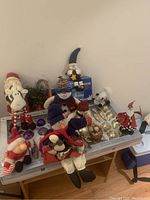 Photo of assorted Christmas plush figures including snowman, Santa, and others placed on a small table.