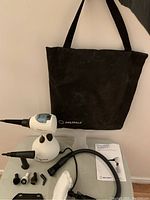 Photo showing the steamer unit, multiple steam head attachments, black carry bag, and manual.