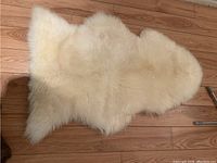 Photo of off-white, natural-shaped sheepskin fleece rug on wooden floor showing wool texture and shape.