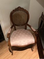 Front angled view of Louis style parlour armchair showing carved wood frame, cane backrest and pink damask seat upholstery