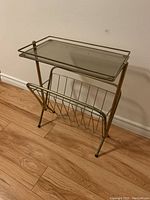 Full view of side table showing steel frame, glass top with metal railings, and magazine rack below.