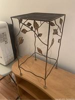 Full view of metal side table showing foliate design on legs, mesh top surface, and overall sturdy structure.