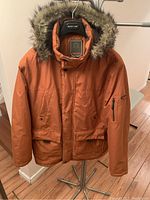 Front view of orange Weatherproof parka with faux fur hood on hanger