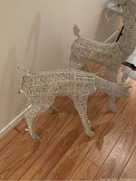 Front and side angle of two white painted steel wireframe reindeer figures with integral lights on a wood floor indoors.