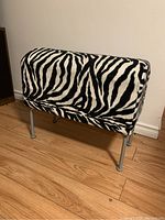 Full front view of Ikea Pastill stool with zebra print upholstery on wooden floor against white wall.