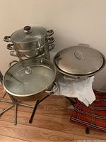 Full view of the cookware set including open wok pan with glass lid, stacked three-tier steamer with glass lid, and large pot with lid.