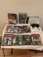 Full view of games and accessories on table including PS2, PS3 and Wii U games, PS3 controller and Wii steering wheel.