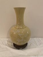 Full front view of the yellow celadon vase on wooden base, showing white enamel floral and bird motifs.