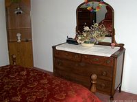 Front view of antique wooden dresser with attached mirror, artificial flowers in ceramic vase, and small decor items on top.