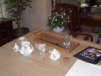 Photo of china tea set and glassware on table with floral centerpiece and wall art