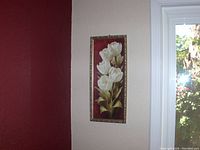 Photo of a framed floral wall picture hung on a white wall next to a red painted wall.