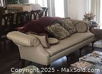 Sofa in a living space showing beige upholstery, rolled arms, decorative pillows, and wooden legs