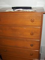 Front view of the wooden dresser showing four drawers with round wooden knobs and wear marks on the surface.