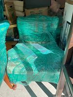 Two high back living room chairs wrapped in green plastic wrap, placed next to each other and surrounded by other boxes and furniture in storage.