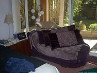 Loveseat sofa with multiple decorative pillows and a throw blanket in a living room setting near sliding glass doors.