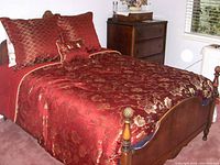 Photo of antique queen size wooden bed frame with carved details and red-gold floral bedding.