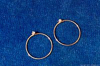 Pair of delicate 10kt yellow gold round hoop earrings with a small clear gemstone near the clasp, set on a blue surface.