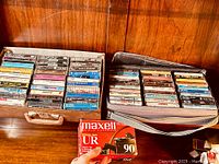 Two cases of vintage rock cassette tapes including Led Zeppelin and Pink Floyd, with near full sealed box of Maxell cassettes in front