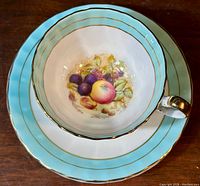 Top view of the teacup placed on the matching saucer, showing the orchard fruits painted inside the cup and the blue-gold border on both pieces.