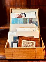 Wooden box containing assorted prints, paintings, and framed artworks arranged standing vertically.