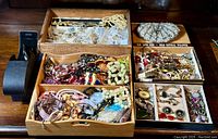 Wide shot showing multiple boxes and trays of assorted estate jewelry including many beaded necklaces and bracelets in different colors and styles.