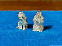 Front view of sterling silver cat and owl charms with green gemstone eyes on blue background.