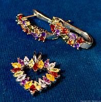 Heart-shaped open pendant and baguette hoop earrings displayed on blue fabric showing multiple colorful gemstones set in sterling silver.