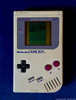 Front of Nintendo GameBoy handheld showing screen with Tetris game playing, buttons and directional pad visible, screen has vertical lines on sides.