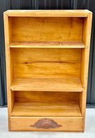 Full view of the pine wood wall shelf showing three shelves and drawer with decorative pull.