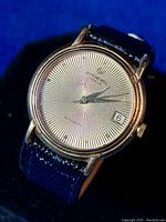 Angle front showing gold-colored dial with radial pattern, gold watch case, missing some diamond markers, black leather strap.