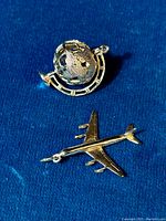 Photo of the two sterling silver charms, one a revolving globe and the other a jet airplane, on a blue fabric background.