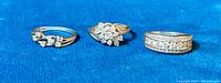 Three sterling silver rings with gold wash and cubic zirconia stones displayed on blue fabric