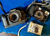 Three vintage Canon cameras together: PowerShot A540, Sure Shot, T80 all visible on blue background