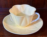 Front angle view of vintage Shelley Dainty teacup and saucer set, showing its pale butter yellow color and blue handle with scalloped edges.