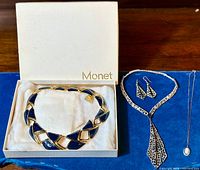 All pieces displayed including original Monet box: primary royal blue enamel necklace in box, silver-tone Y-necklace, earrings, and pendant necklace on blue background.