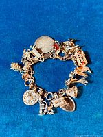 Full view of vintage charm bracelet on blue fabric background showing detailed sterling silver and enamel charms.