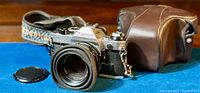 Canon AE-1 Program 35mm film camera with leather case and neckstrap on blue surface