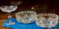 Three pieces of cut crystal on a blue cloth: one compote with pedestal and diamond lattice bowl, two matching bowls with starburst cuts.