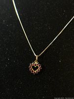 Close-up of the heart-shaped garnet pendant with faceted stones on a black background showing the stone detail and silver setting.