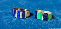 Two rings side-by-side showing lapis lazuli inlay on one ring and lapis lazuli with malachite inlay on the other.