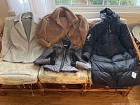 Four coats displayed on a chair including grey Zara coat, brown teddy coat, black padded kangol winter coat, and black Blanc Noir moto jacket.