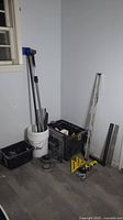 Photo showing rolling tool box, plastic buckets with poles, large spirit level, some black tool crates, and measuring squares on floor.