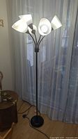 Full view of the black metal floor lamp with five white lampshades standing near a window.