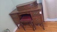 Full view of the antique wooden vanity dresser with stool pushed underneath.