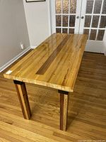 Angled side view showing butcher block top, leg design, and brackets in a room with hardwood floor and French doors.