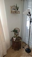 Full view of Indian wood carved foldable table with potted green plants and small decorative rattan chair on top, next to curtain and lamp (not included).