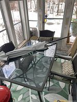 Metal framed rectangular patio table with clear glass top and four matching metal framed chairs with cushions, green and white leaf patterned floor mat beneath