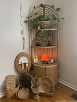 Full view of corner shelving unit with pothos plant, Himalayan salt lamp, wicker baskets, mirror, rattan wine rack, Chinese painted glass globe, candles, and decorative items.
