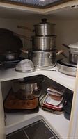Corner cabinet filled with various pots, pans, baking dishes and baking pans stacked and organized.
